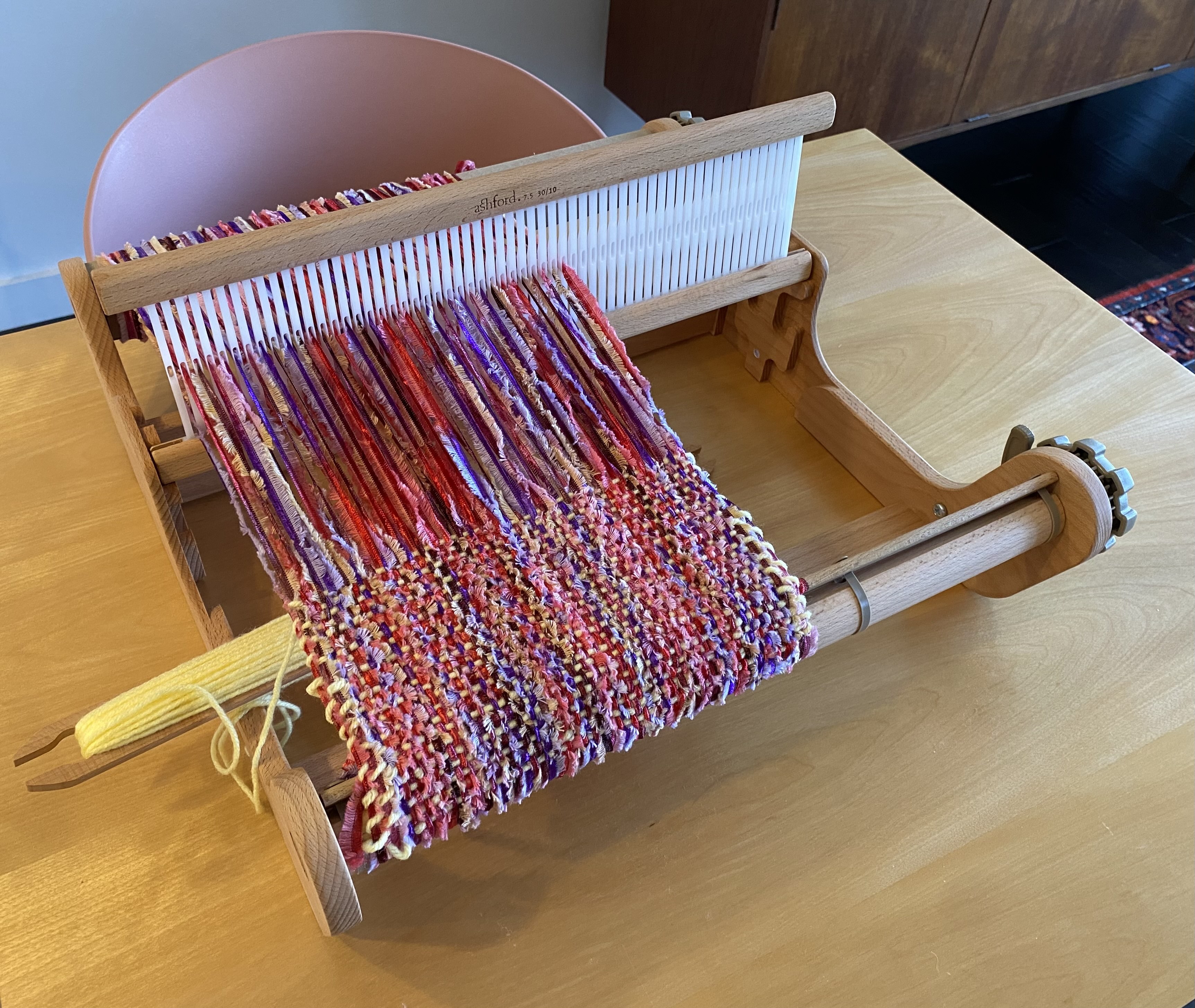 A loom set up on the dining room table with multicolored yarn.